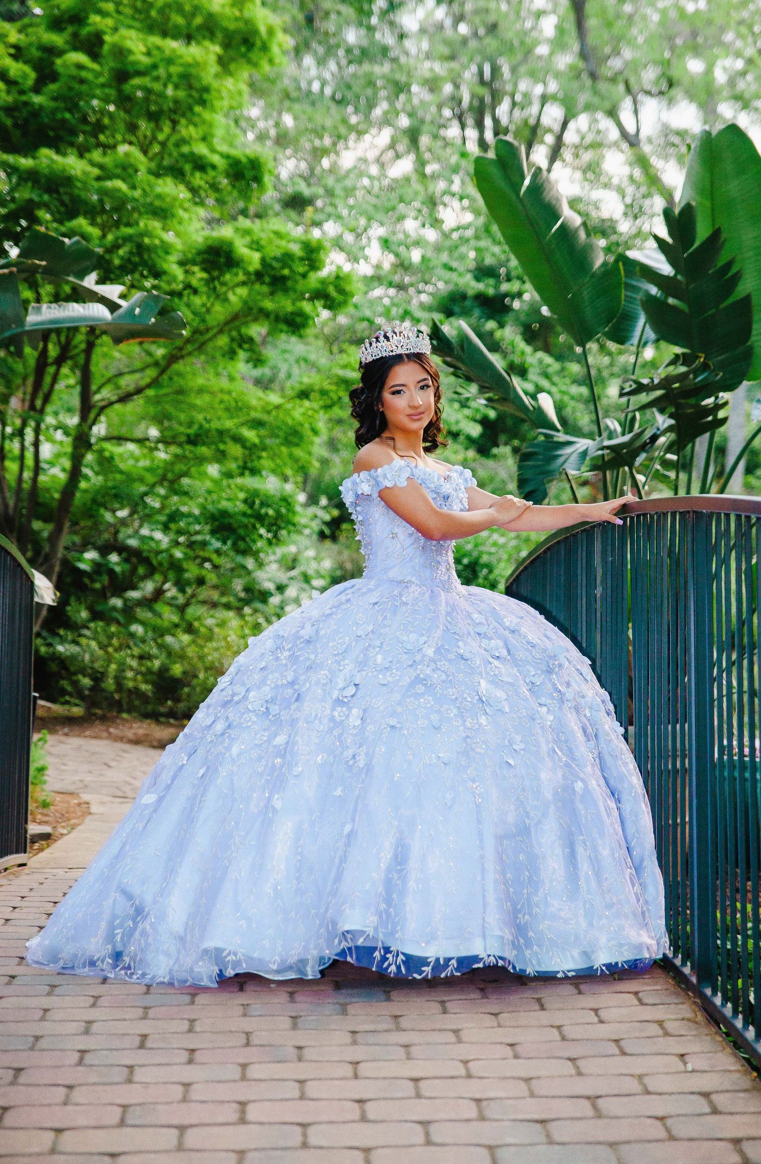 Quinceañera portrait in white ball gown on garden path with tropical foliage.