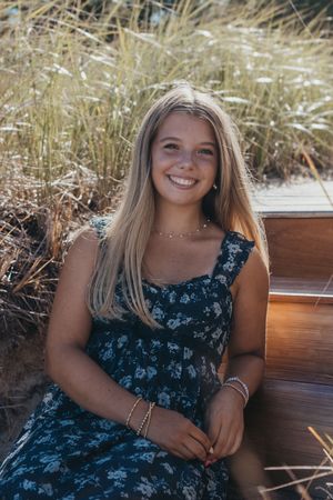 A summer portrait of a person in a floral blue sundress sitting outdoors among tall grass.
