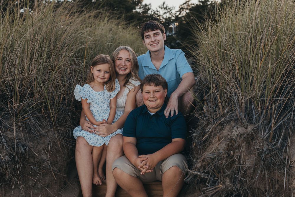 Casual outdoor family portrait among tall beach grass at dusk.
