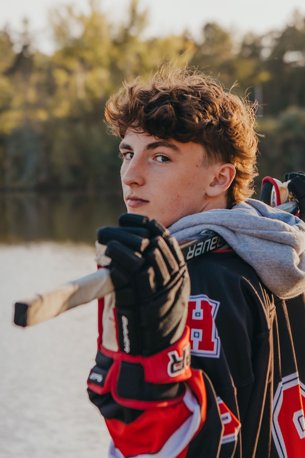 A hockey player in protective gear poses against a sunset lake backdrop.