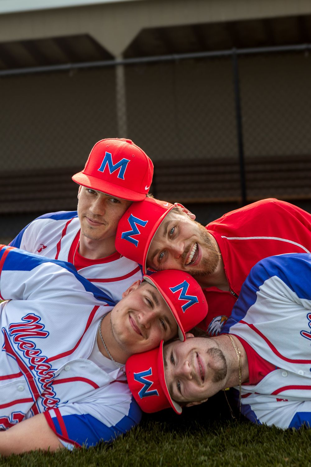Four smiling baseball players in red and white uniforms with M caps pose together lying on grass.