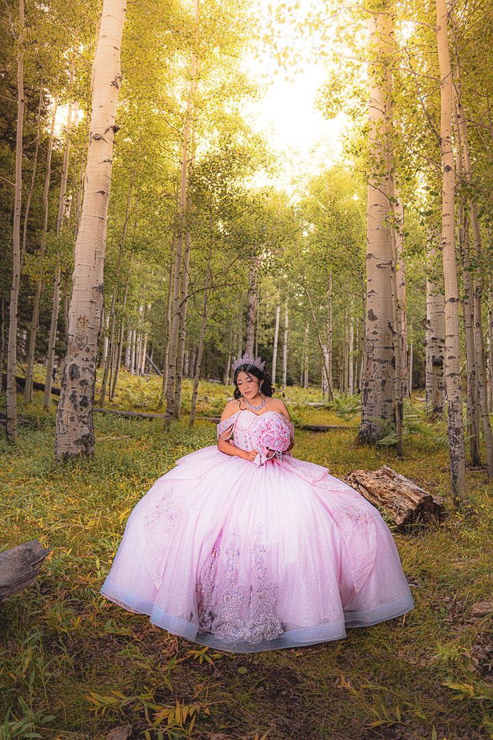 A pink ballgown dress stands out against a golden aspen forest during sunset, creating a dreamy woodland scene.