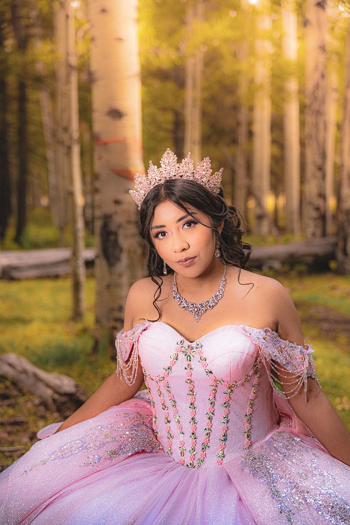 A pink quinceañera dress sparkles in an aspen forest during golden hour with delicate embellishments and flowing tulle.