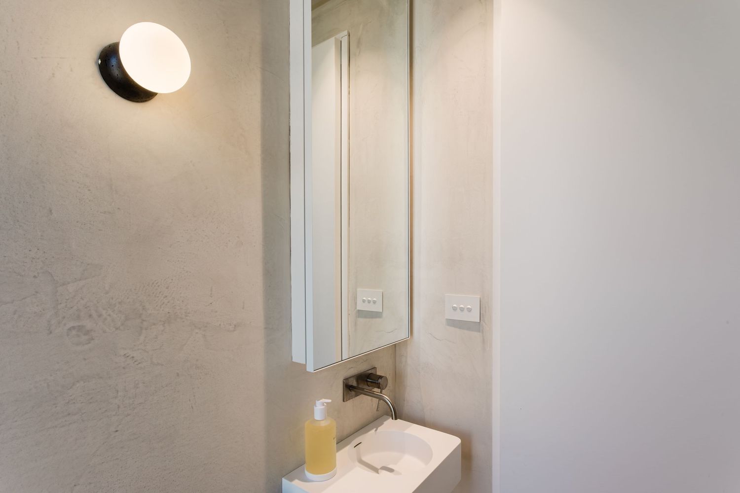 Modern minimalist bathroom interior with concrete walls, black framed window, and white fixtures.