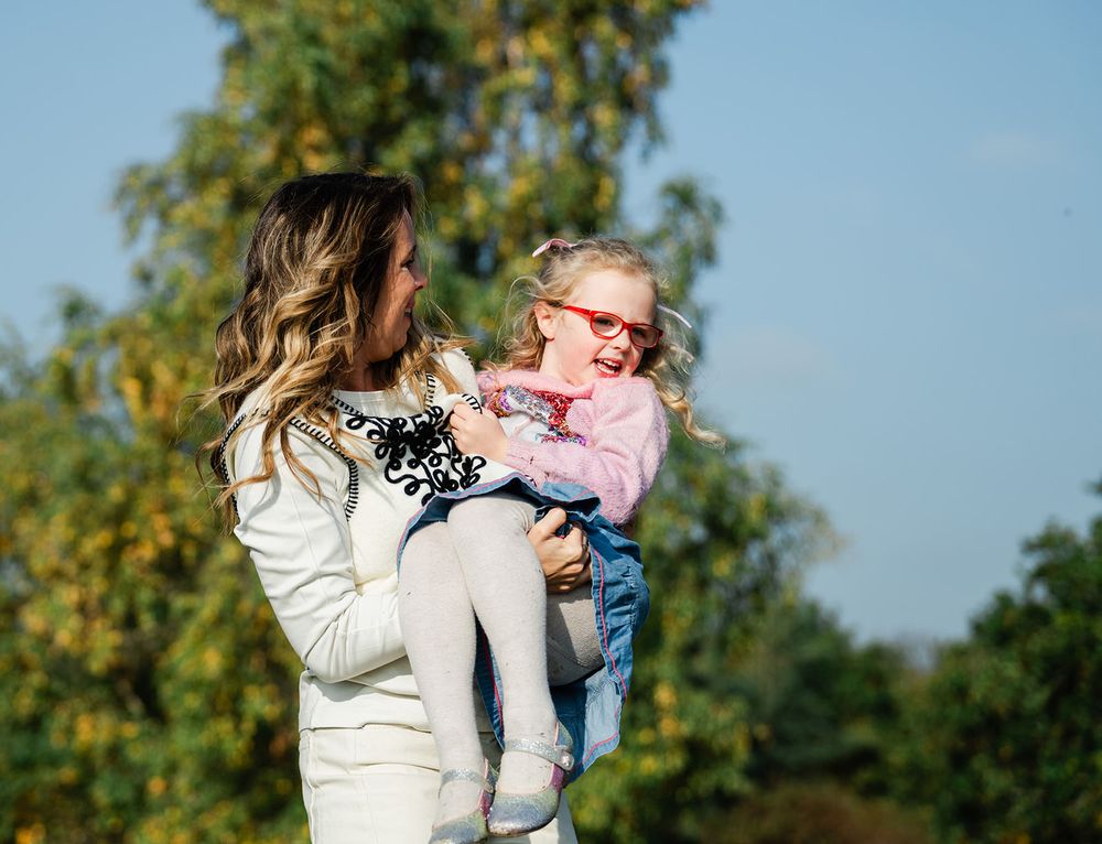 A parent and child share a tender moment together outdoors on a sunny autumn day with trees in the background.
