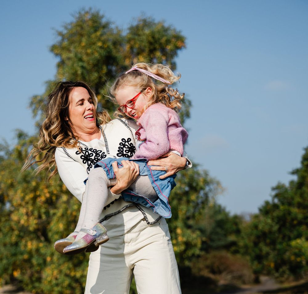 Mother and child embrace joyfully in an outdoor setting with autumn trees in the background.