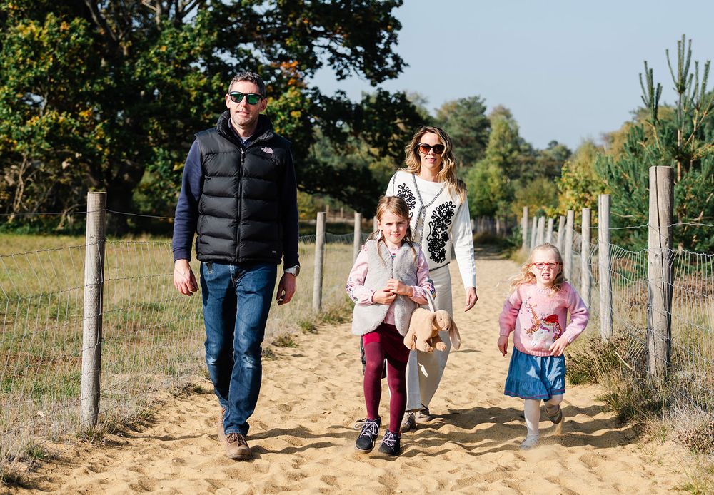 A group of people walking along a sandy path bordered by wooden fence posts on a sunny autumn day.