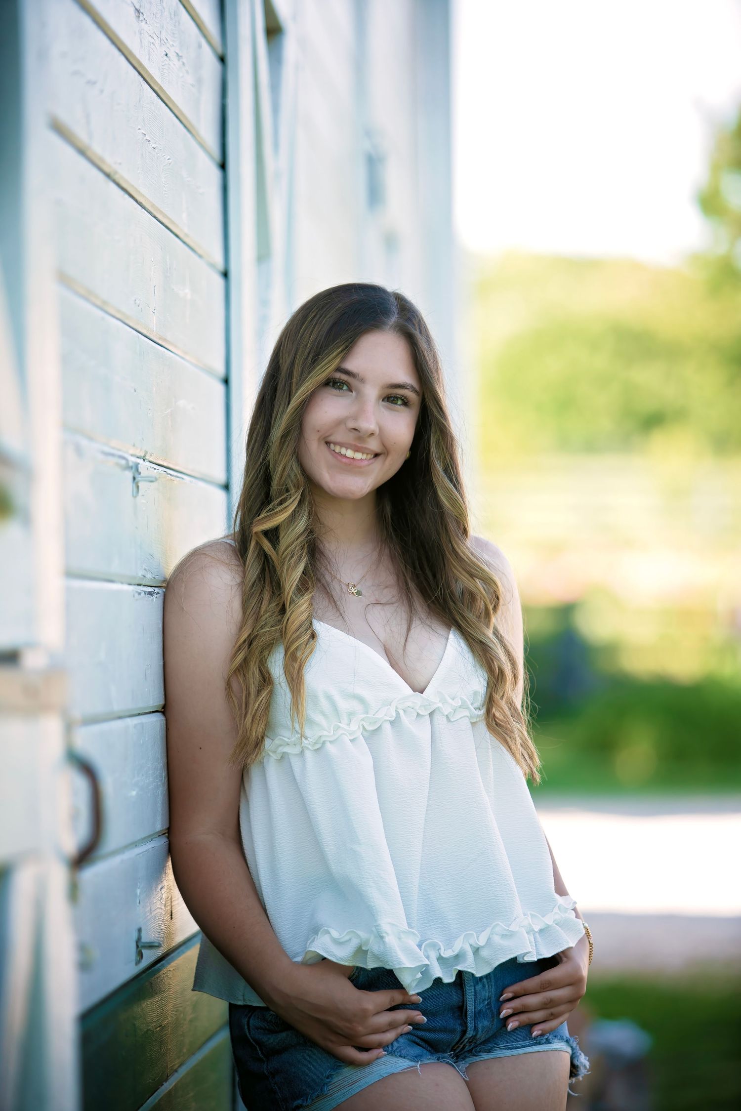 Senior portrait session against white wall featuring casual summer outfit and natural lighting.