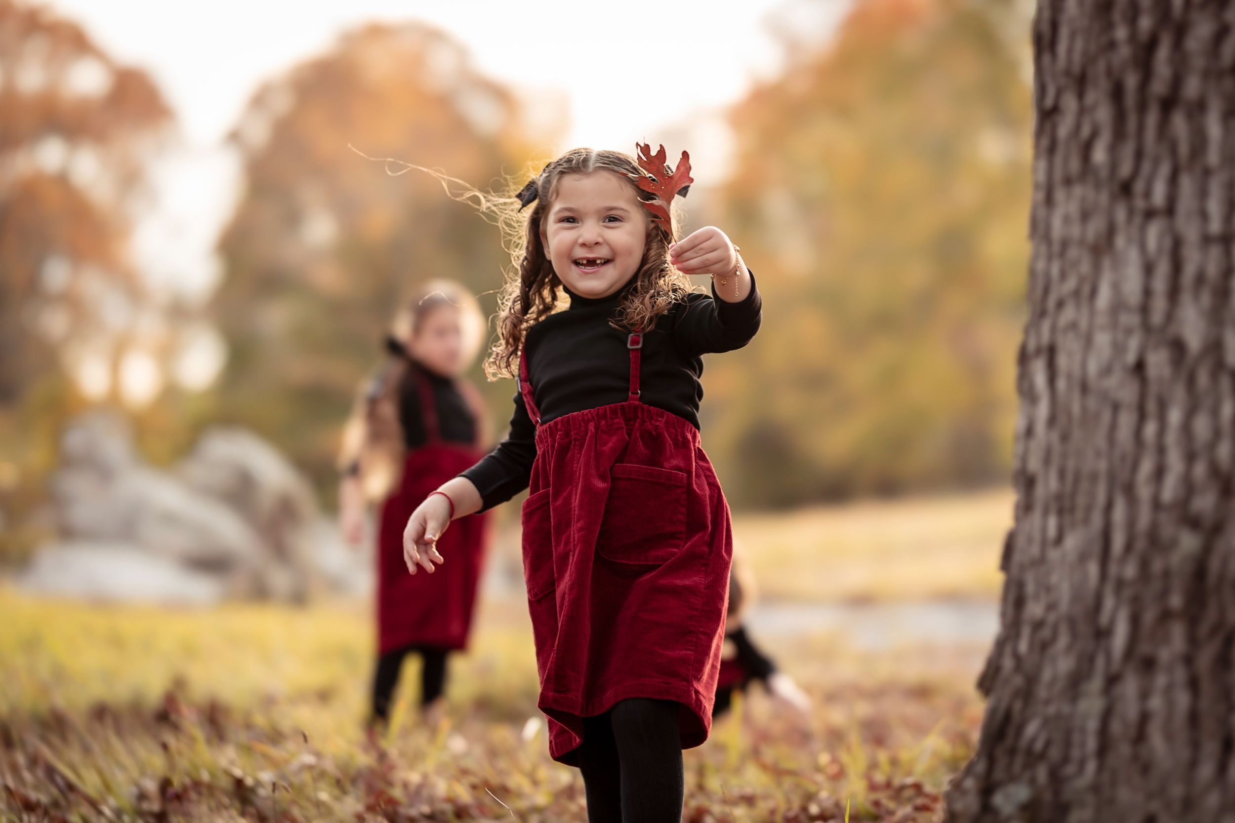People in matching burgundy velvet outfits play together outdoors on a fall day.
