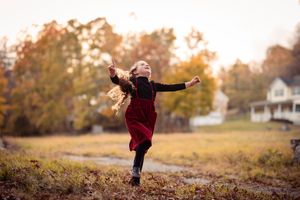A person in a burgundy sweater leaps joyfully through a golden autumn field at sunset.