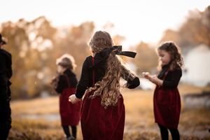 A group of people in burgundy sweaters stand together during golden hour in an autumn outdoor setting.