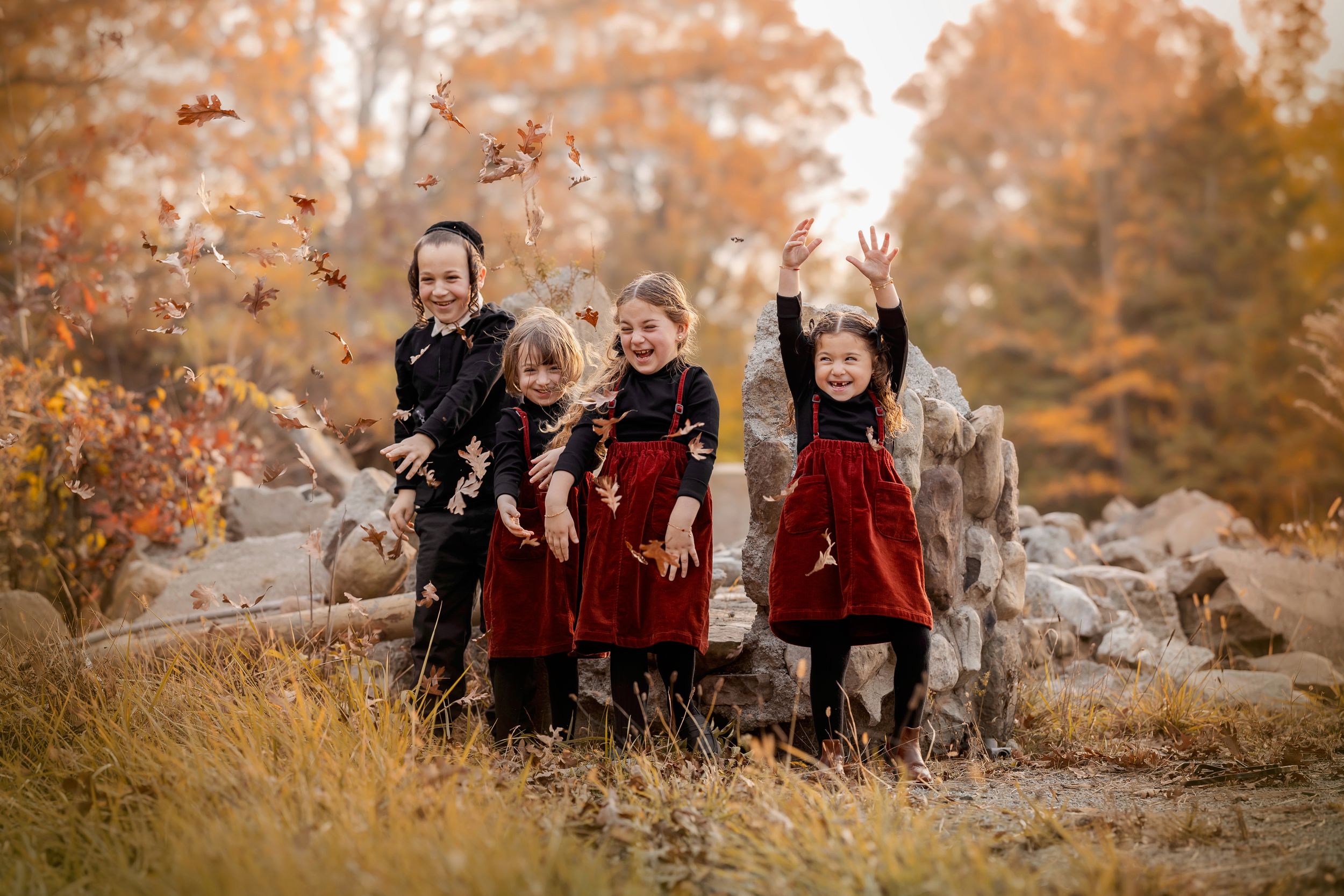 A family group poses together on rocks surrounded by autumn foliage in warm golden tones during an outdoor photo session.