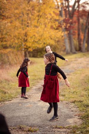 A series of images showing a small figure in a red velvet dress twirling and playing on an autumn path surrounded by golden trees.
