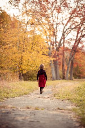 A person in a red coat walks down a leaf-covered autumn path surrounded by golden trees at sunset.