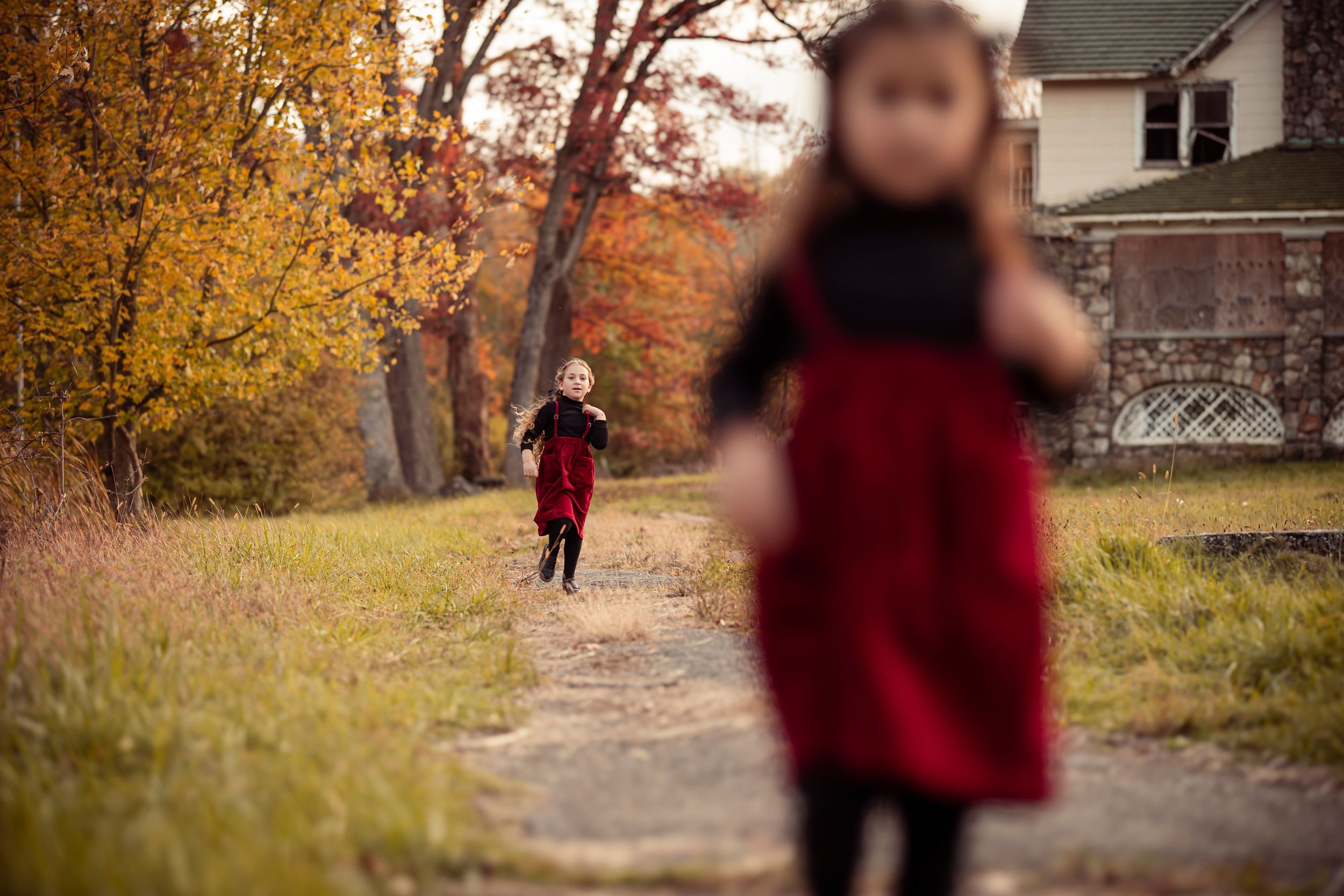 A figure in a red coat walks along a serene autumn path lined with golden trees and fallen leaves.