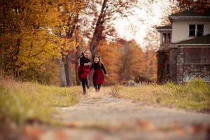 A couple walks together on a tree-lined path during autumn with golden foliage overhead and scattered leaves on the ground.