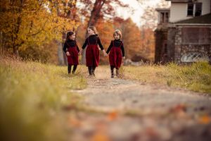 Three people walk along a path surrounded by vibrant autumn foliage and fallen leaves in a park setting.