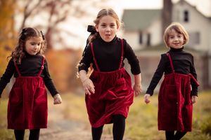 A child in a red velvet dress and black boots runs and plays in an autumn outdoor setting.