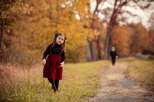 A figure in a red dress walks along a winding autumn path surrounded by golden trees and fallen leaves.