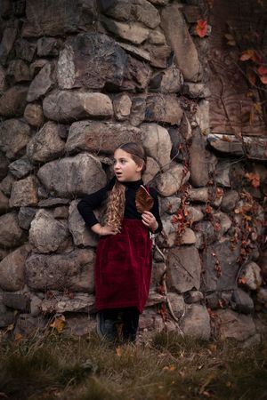 A person in a burgundy sweater sits against a rustic stone wall in an artistic portrait series.