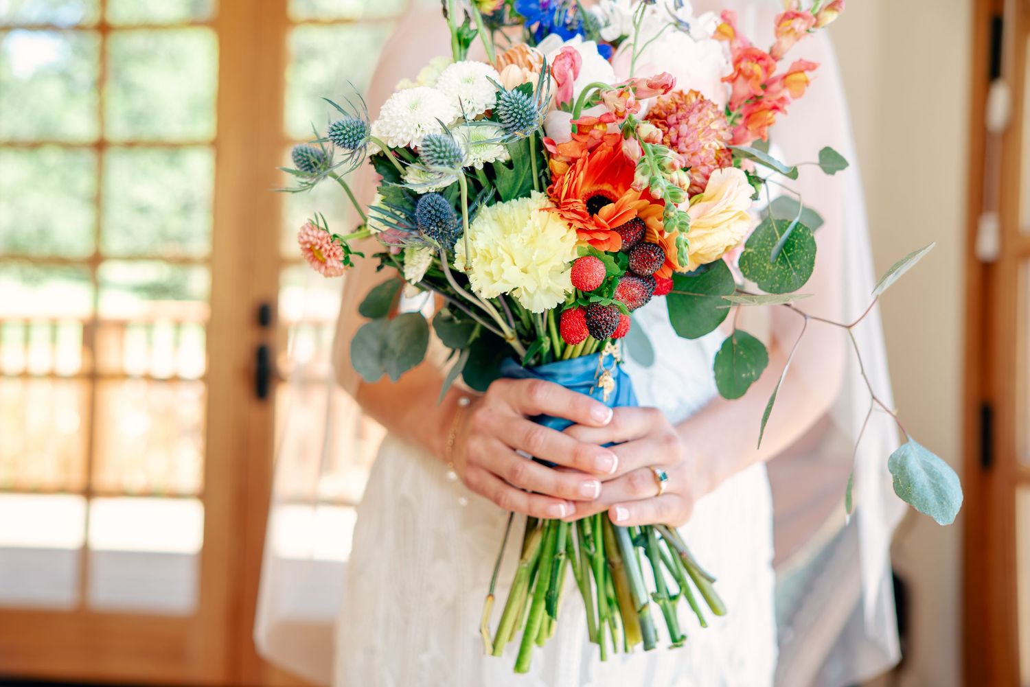 Vibrant wedding bouquets with mixed flowers and greenery held against window light.