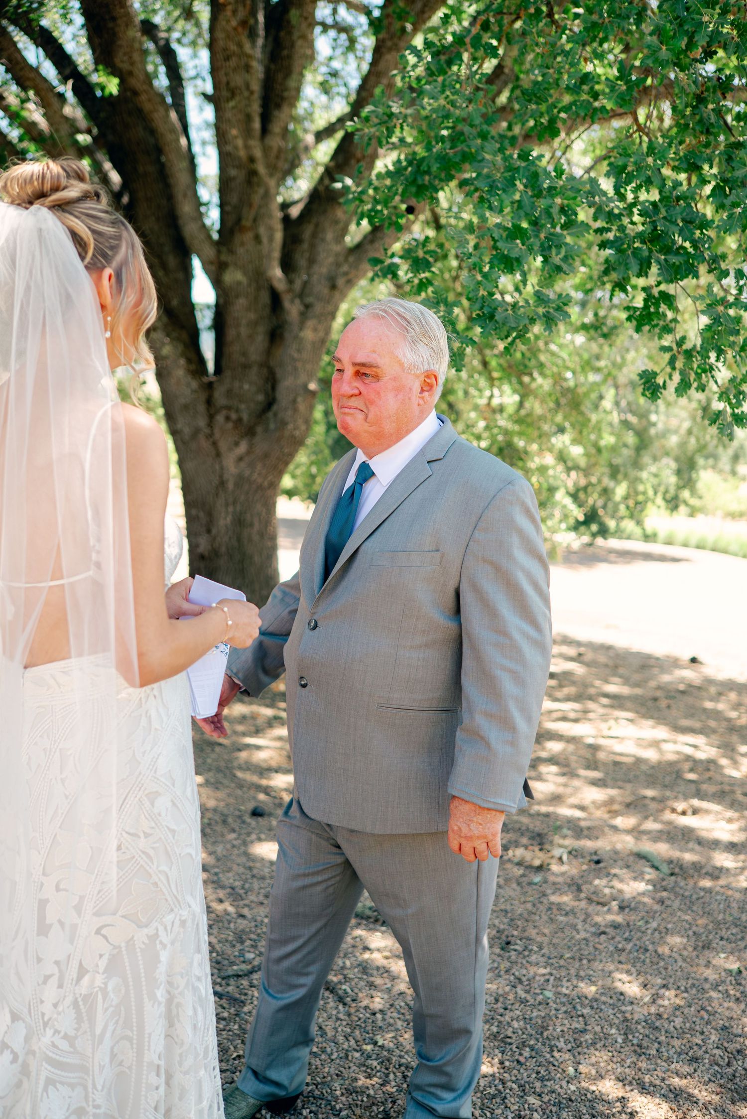 Emotional first look wedding moment captured under shady trees.