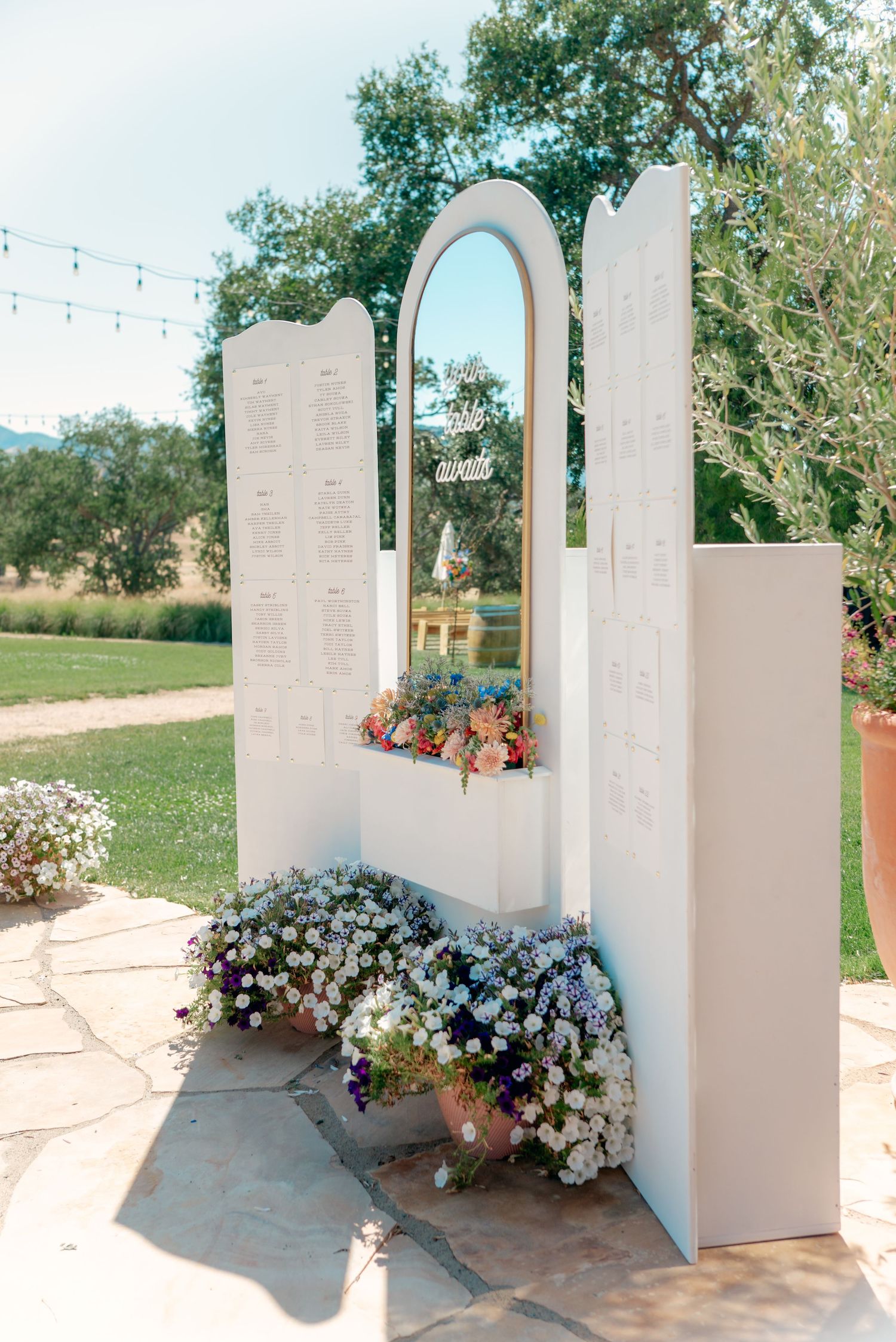 White architectural wedding arch decorated with colorful flowers and greenery.
