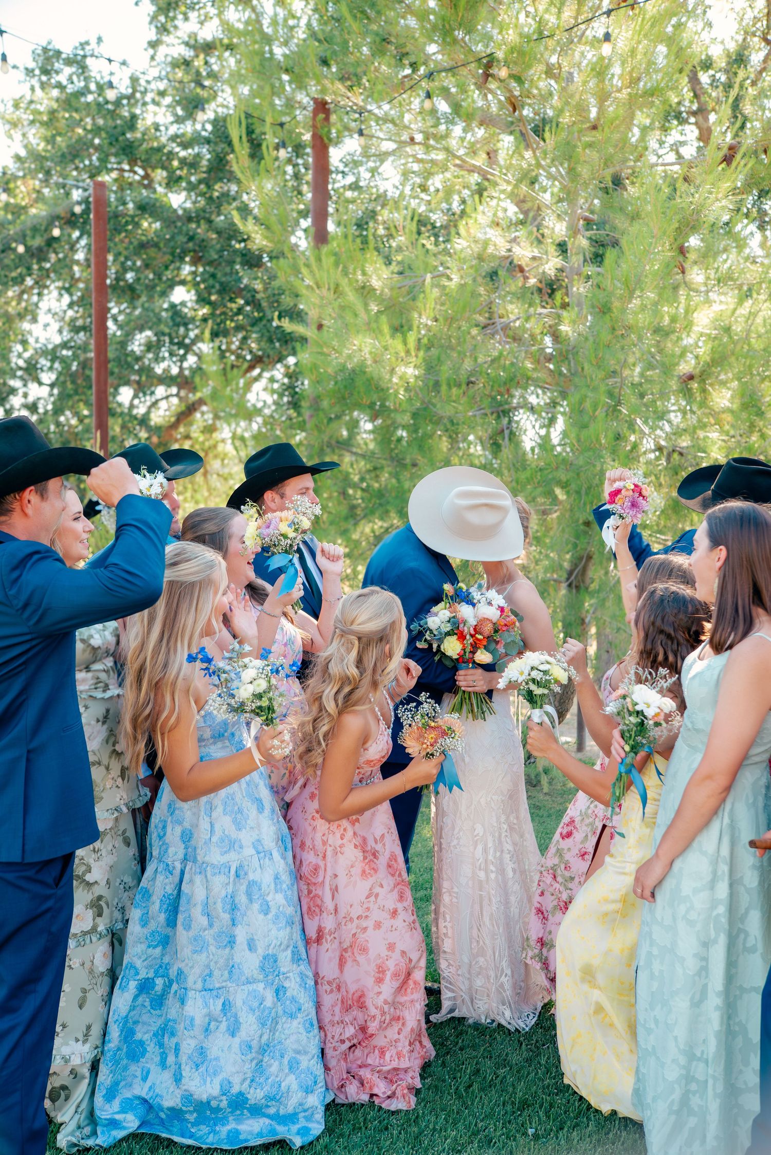 Wedding party in blue suits and floral dresses celebrating with champagne outdoors.