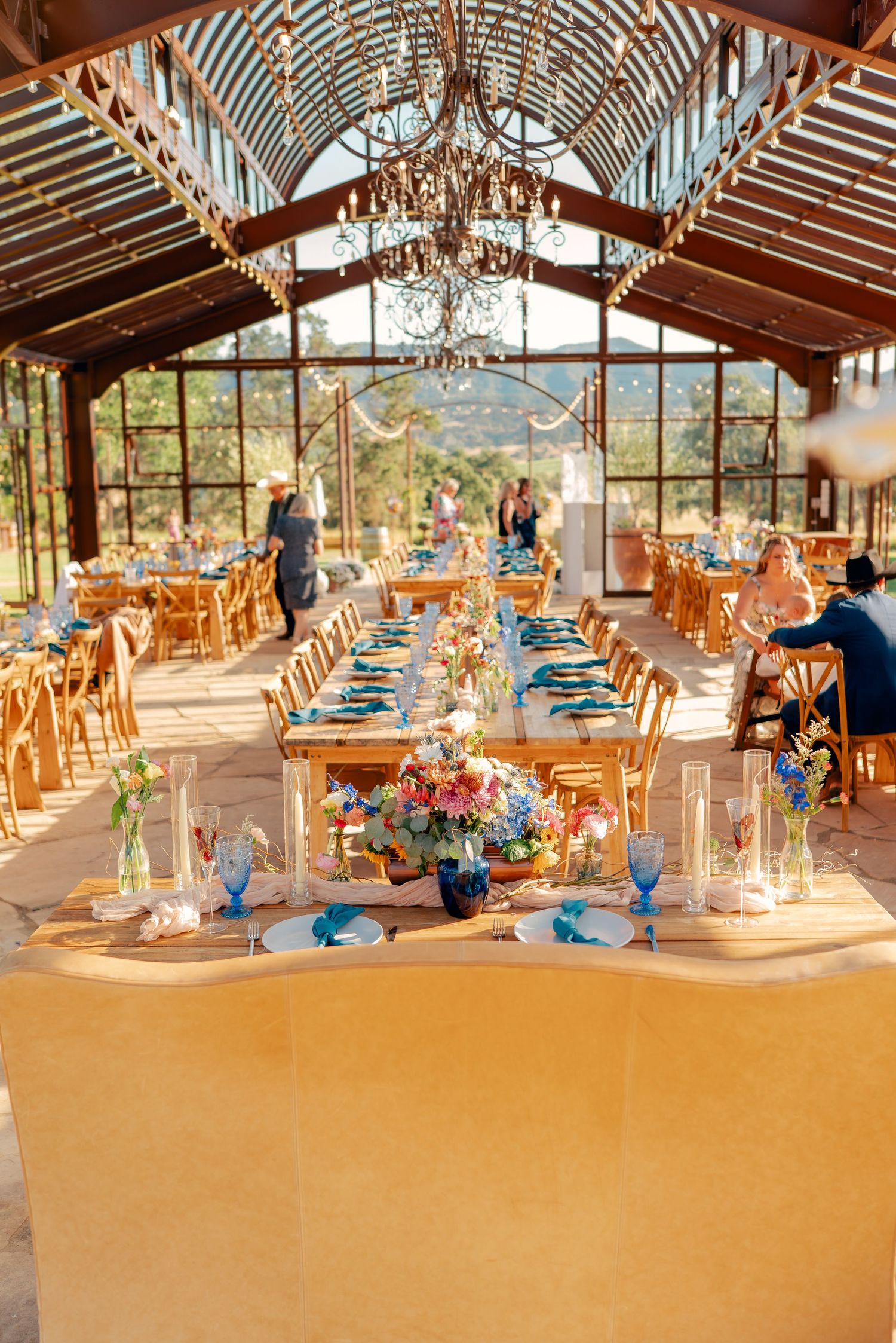 Rustic greenhouse wedding reception with elegant table settings and chandeliers.