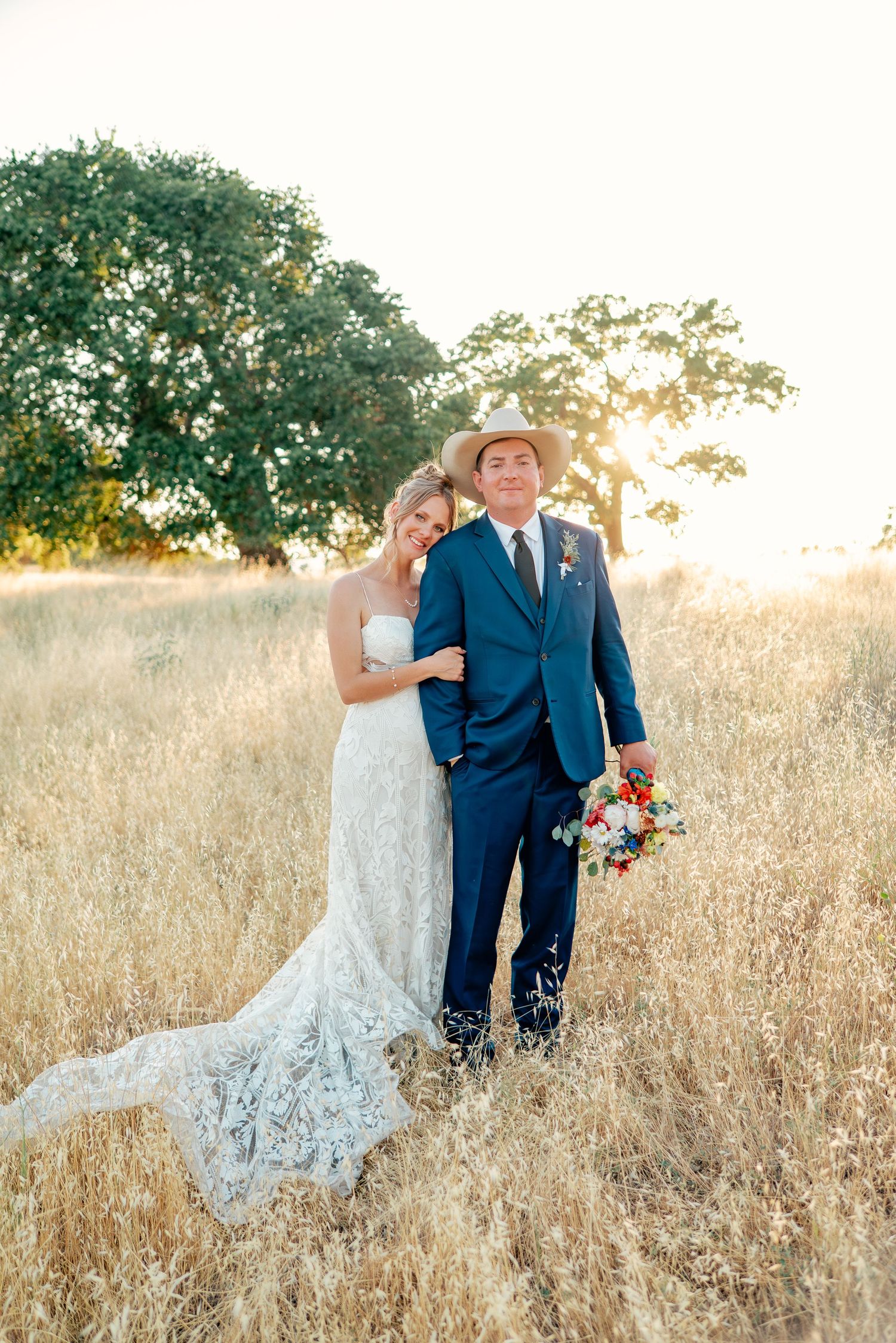 Couple poses in golden field during sunset at rustic outdoor wedding.