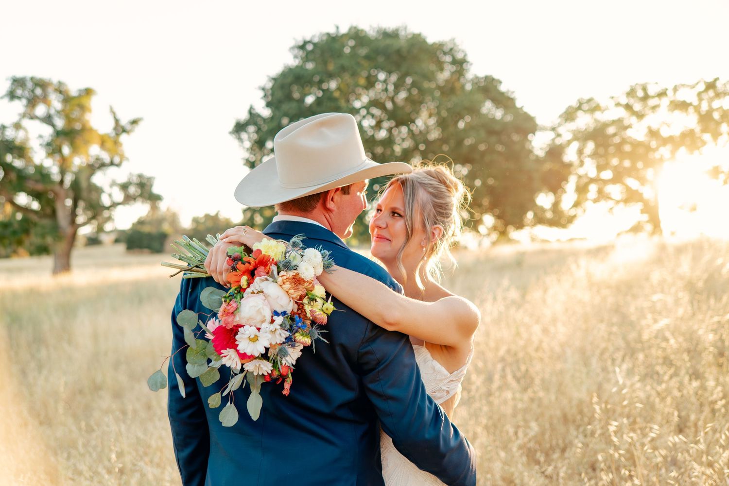 A romantic couple embraces in a sun-drenched field during their wedding day.