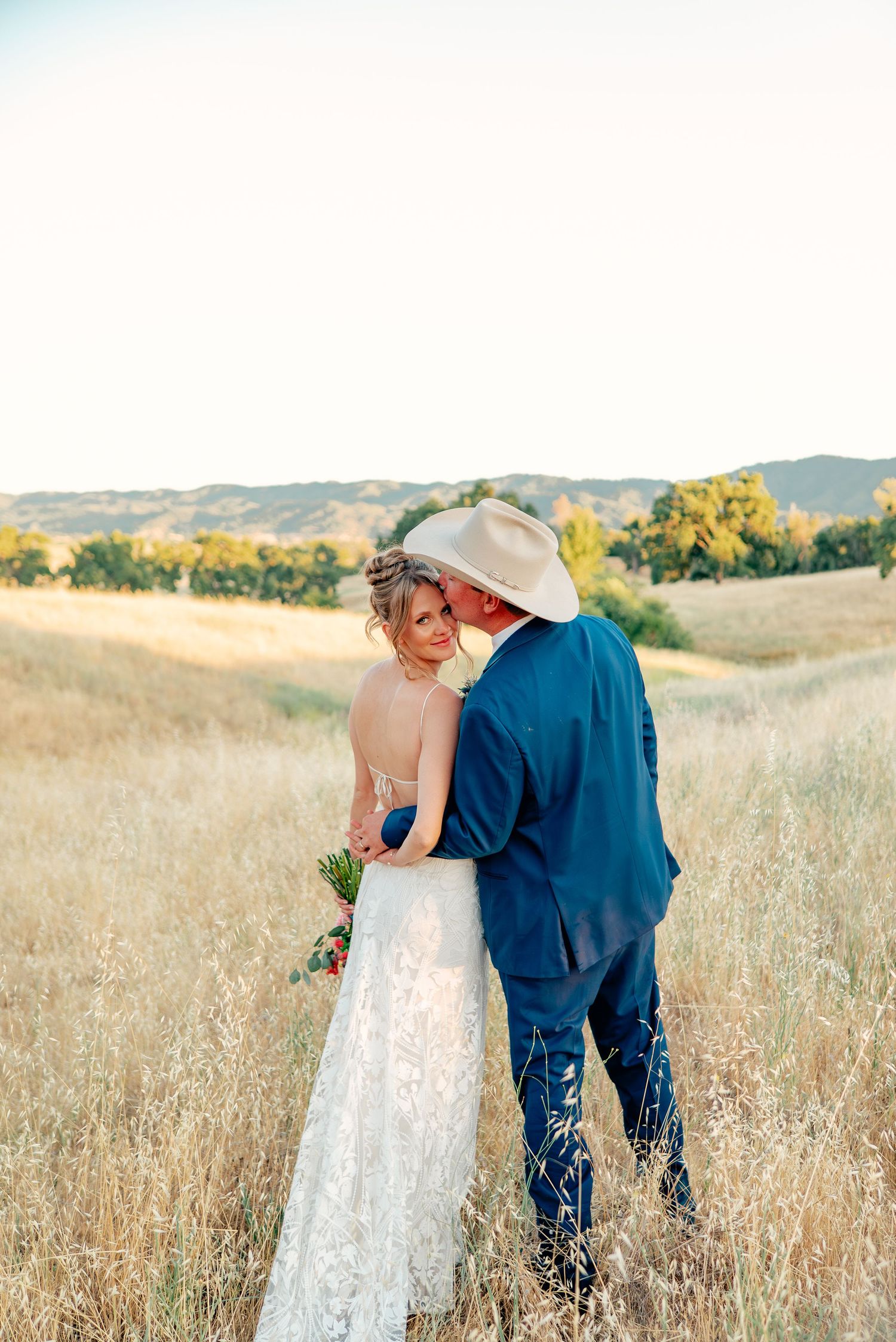 A couple shares an intimate moment in a rustic field during golden hour.