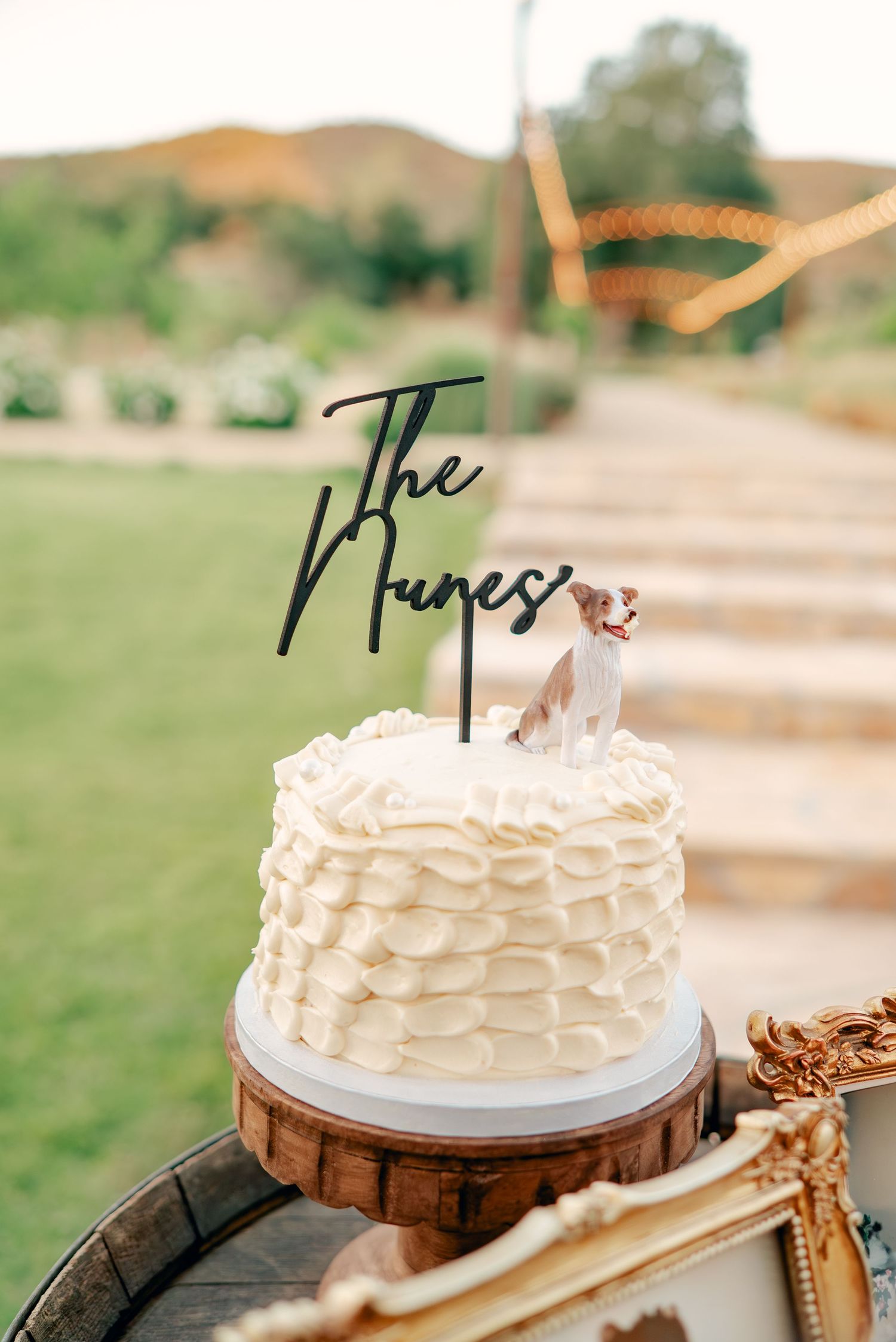 White wedding cake with ruffled frosting details displayed on a wooden stand.