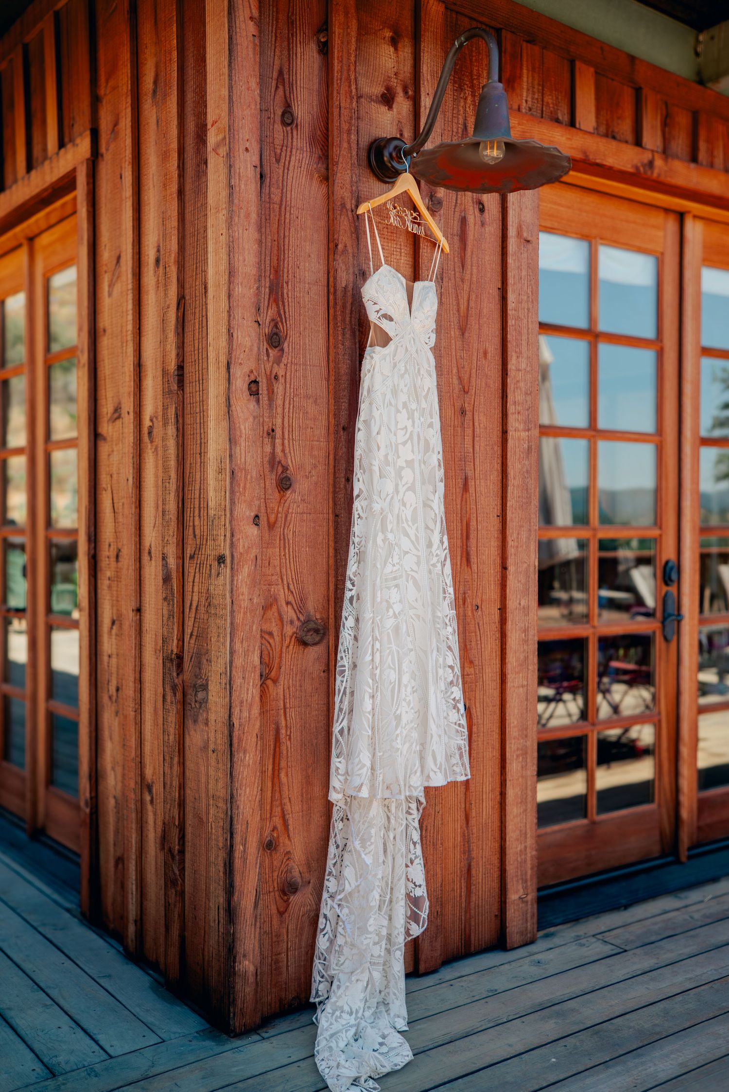 White lace wedding dress hanging on rustic wooden porch panels with natural lighting.