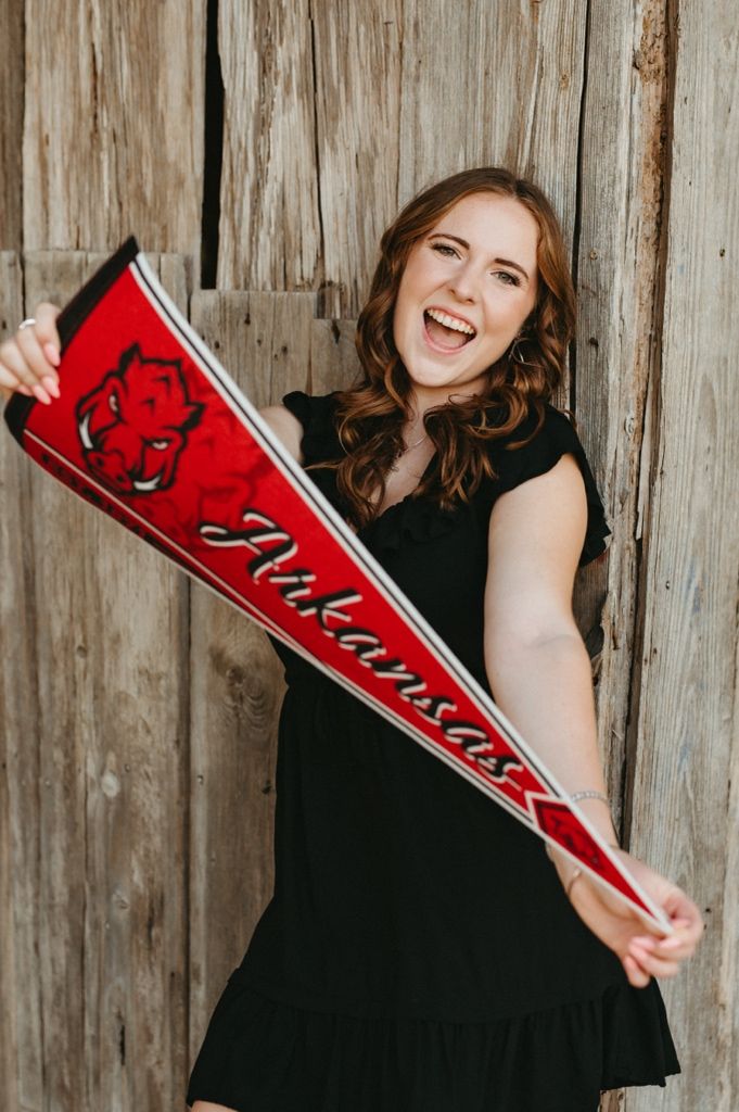 Cheerful person in black dress holds red sports pennant flag against rustic wooden wall backdrop.