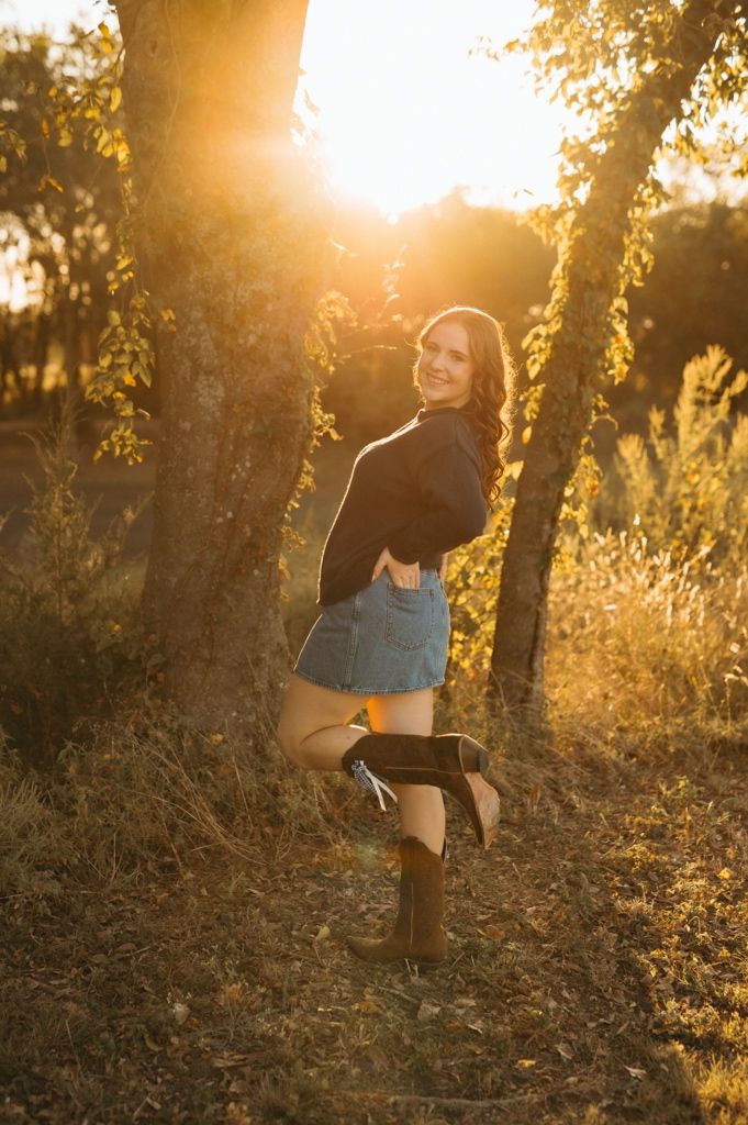 A person sits on a tree branch in a forest bathed in warm golden sunlight during sunset.