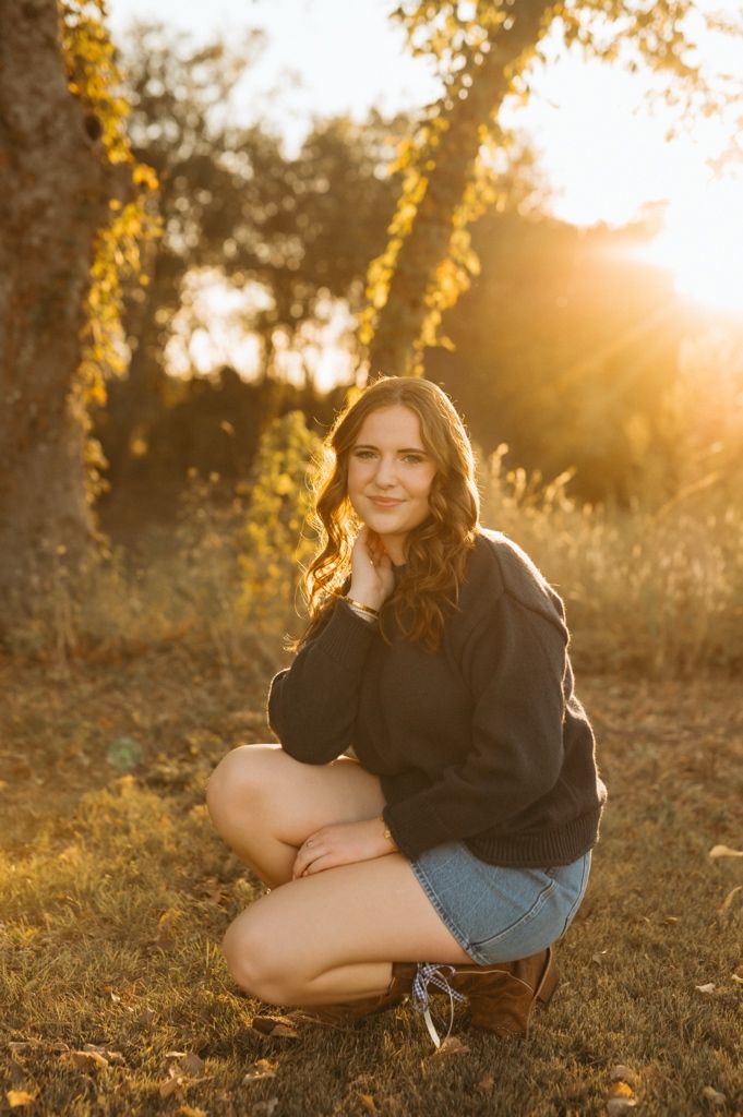 A golden sunset photoshoot in a grassy field with trees casting warm light through autumn leaves.