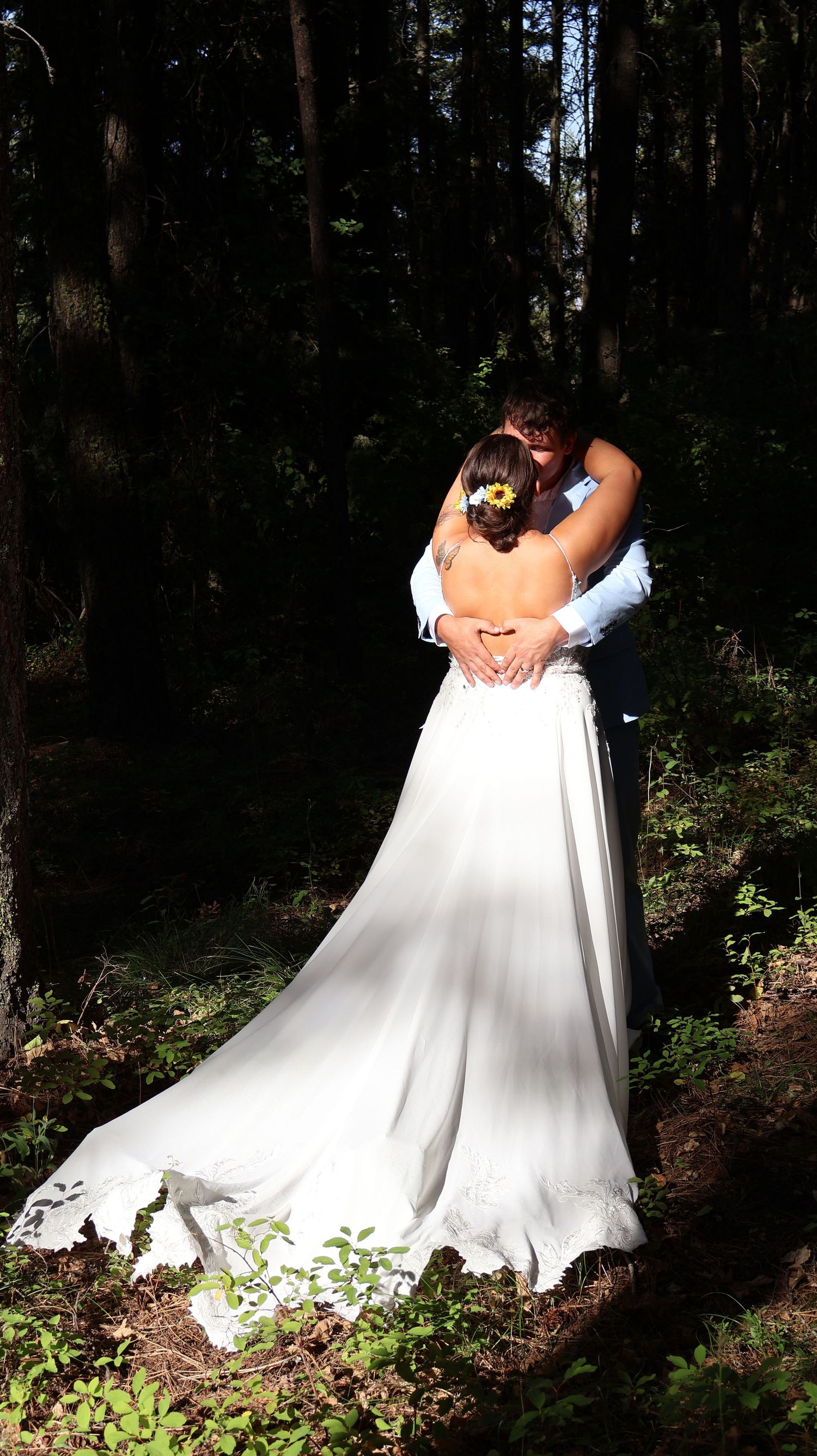 Elegant white wedding dress photographed in a wooded forest setting with dramatic lighting.
