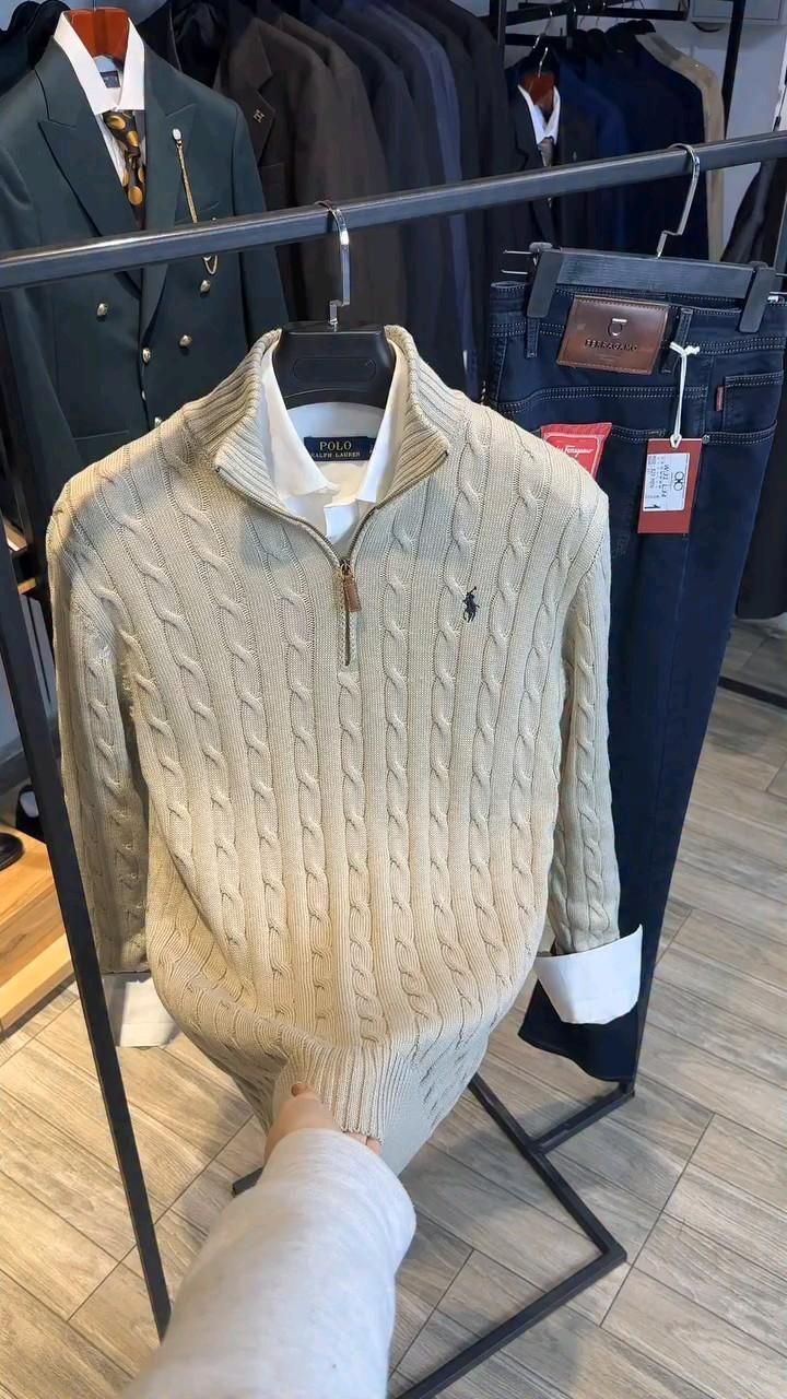 Cream colored cable knit sweater with brown leather collar detail displayed on clothing rack in retail store.