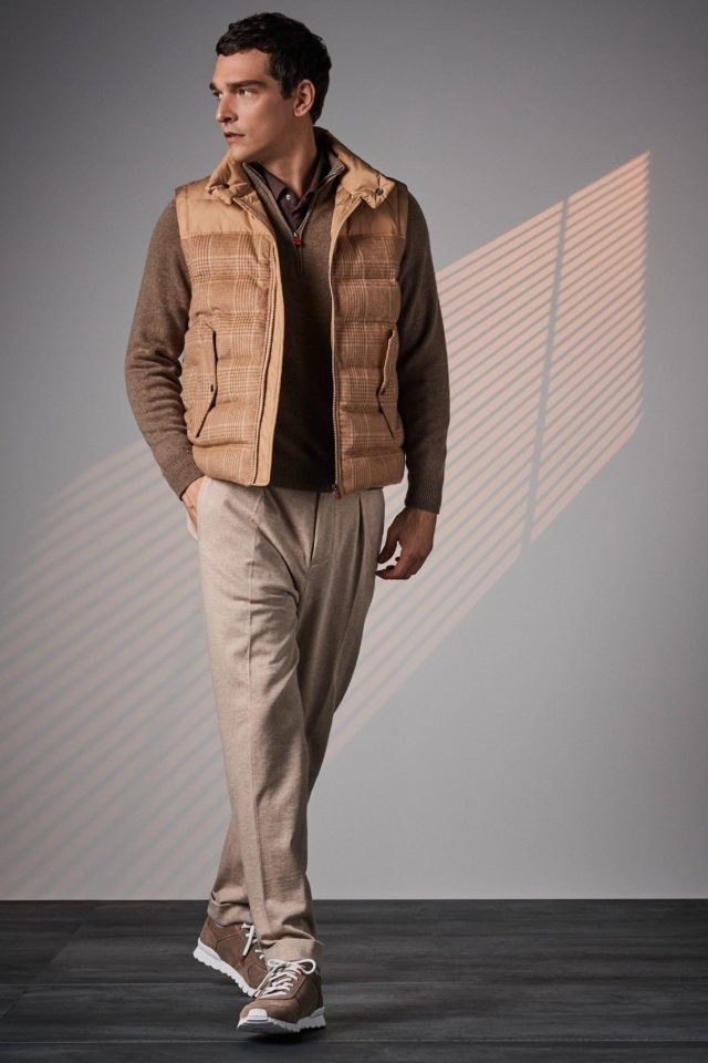 Stylish winter outfit featuring tan puffer vest, brown sweater and light gray trousers with sneakers.