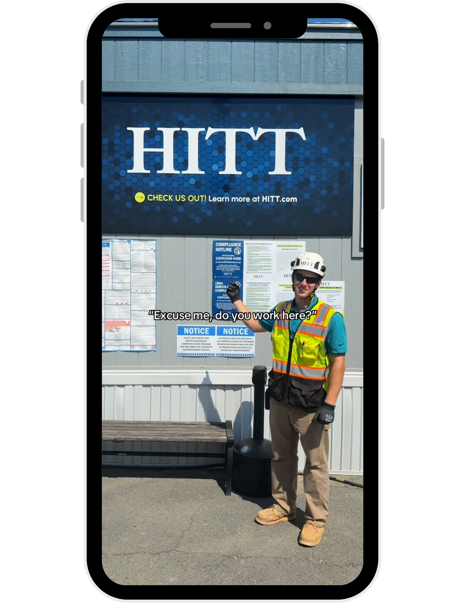 Construction worker in safety gear stands in front of HITT company signage and bulletin board display.