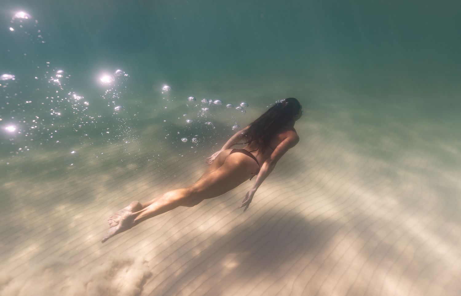 Pregnant woman floating gracefully underwater at Coolum Beach during maternity photoshoot