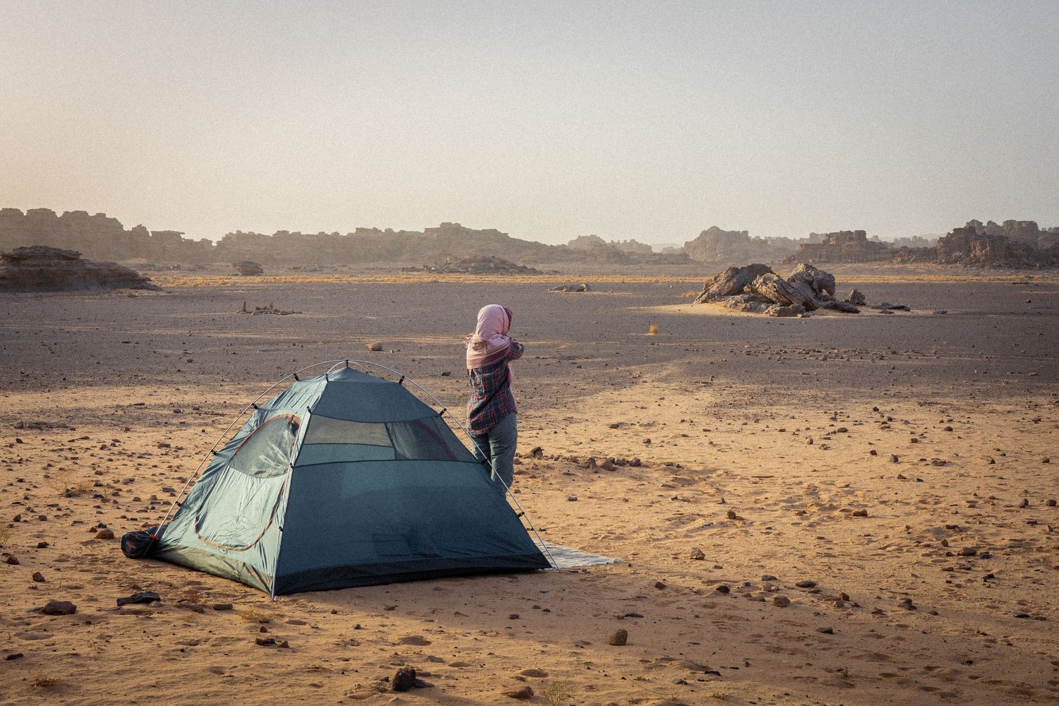 Desert camping scene with tents set up on sandy terrain against distant mountains.