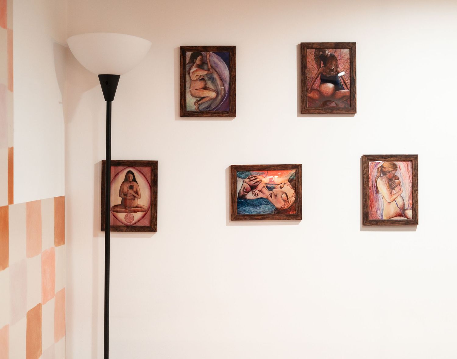 A white wall decorated with five framed artistic prints and a tall black floor lamp in the corner.
