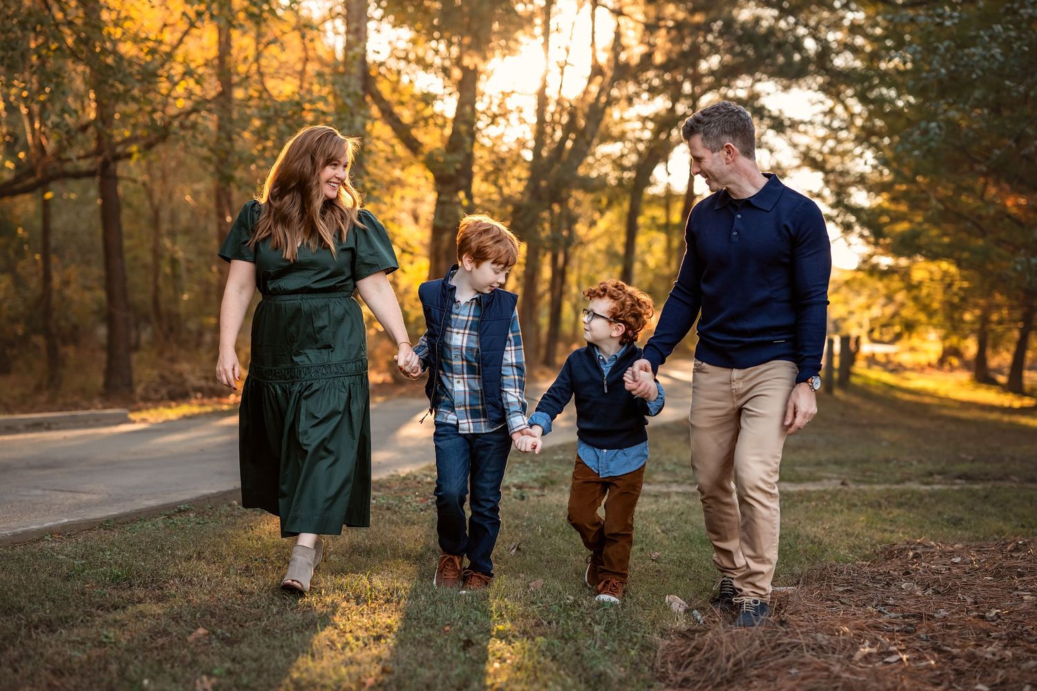 family of 4 walks in the woods holding hands at sunset.