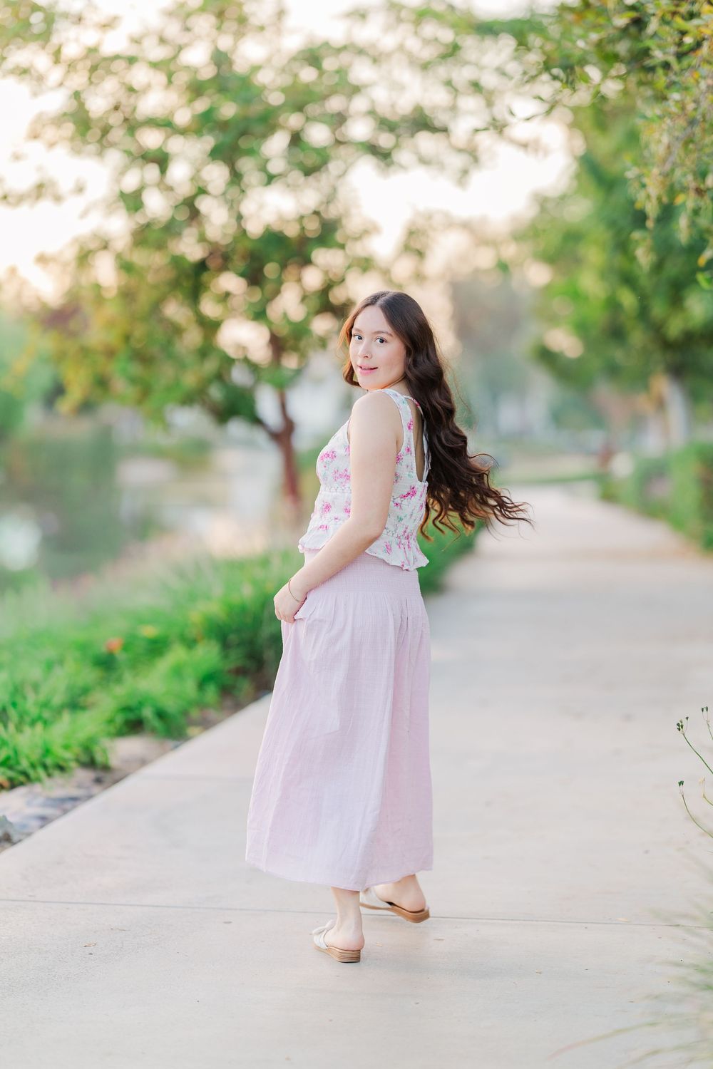 Someone wearing a flowing pink dress twirls and poses on a path surrounded by greenery.