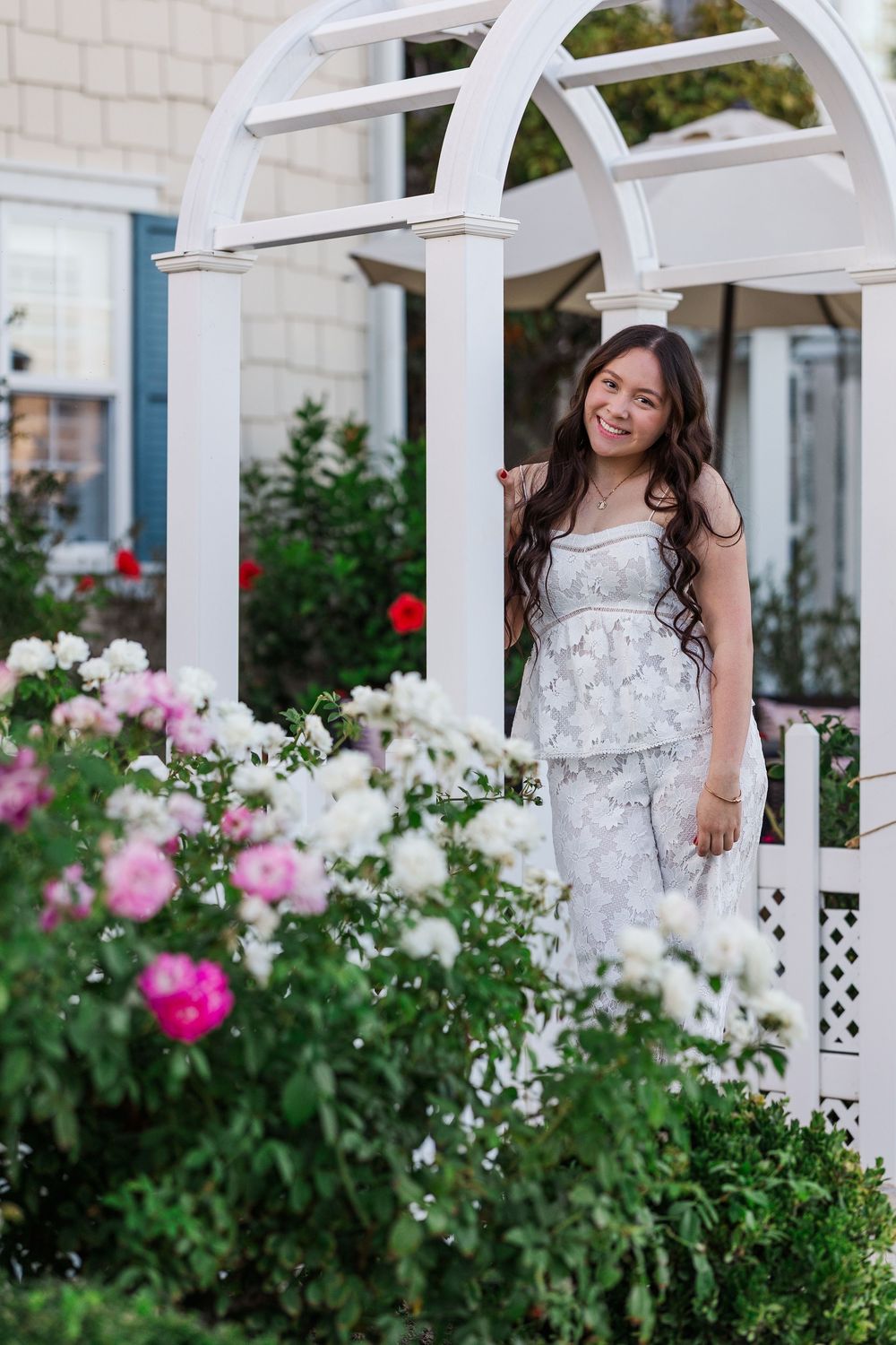 White dress against a garden pergola with blooming roses and greenery in an elegant outdoor setting.