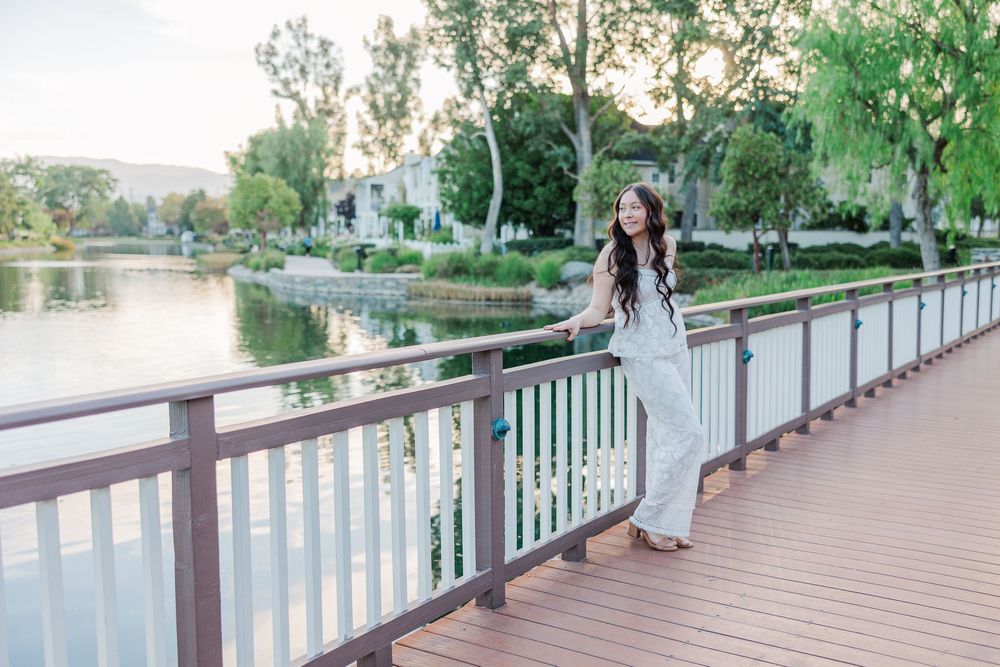 A scenic walkway with wooden railings along a waterfront surrounded by lush greenery.