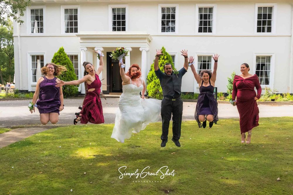 The bride, man of honour and bridesmaids jumping for joy in front of Eastwood Hall.