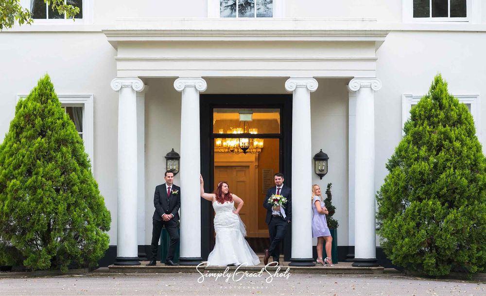The bride, groom, best man and best man's wife pose for a photograph leaning up against the pillars in the entrance to Eastwood Hall.